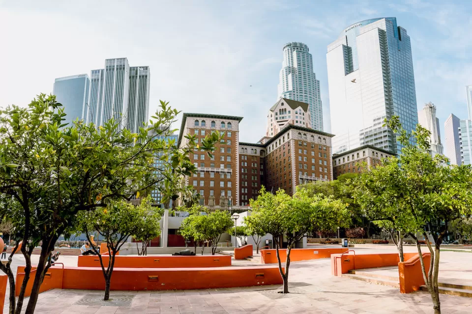 A hardscaped park with creative architectural featues is shown with the high-rises of Downtown Los Angeles in the background.
